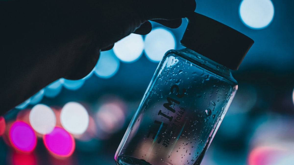person holding clear glass bottle with water